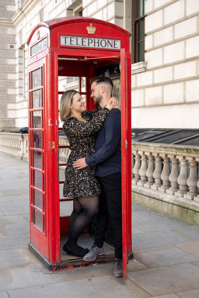 Esküvői fotós Londonban -Wedding photography in England - Egy szerelmes pár meghitt pillanata egy klasszikus piros telefonfülkében. Egyedi és romantikus jegyesfotózás esküvői emlékekhez.