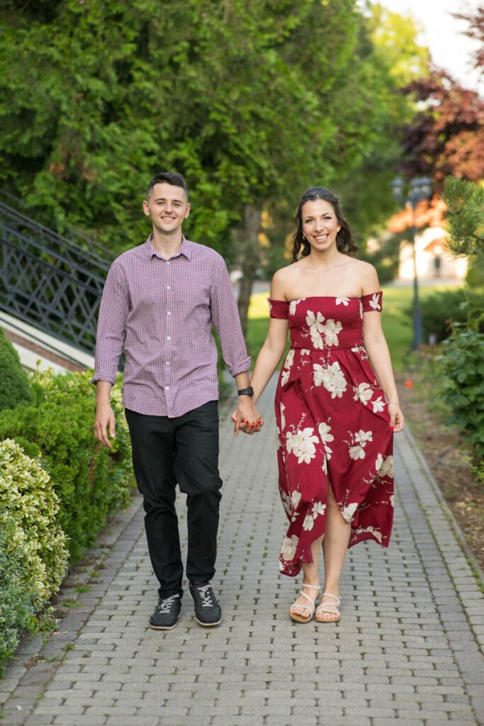 Esküvői fotós jegyesfotózása az Erdőspusztán – Egy boldog szerelmes pár kéz a kézben sétál egy hangulatos, zöld növényzettel övezett úton. Professzionális esküvői fényképész által készített természetes és érzelemdús páros fotók az esküvő előtti különleges emlékekhez.