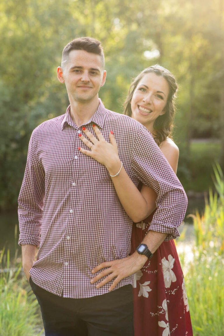 Esküvői fényképész által készített romantikus jegyesfotó, amelyen a menyasszony boldogan öleli vőlegényét, miközben büszkén mutatja eljegyzési gyűrűjét. A természetes fény és a zöld háttér varázslatos hangulatot teremt, tökéletes pillanat egy esküvői fotós számára. Tóth Pálma szertartásvezető boldogan készül a nagy napra.