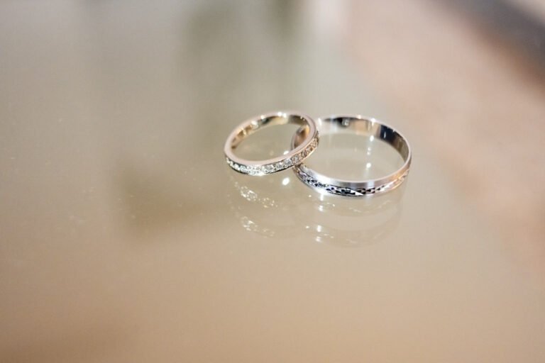 Elegáns esküvői csendélet fehér márvány asztalon, Pol Roger pezsgősüveg, három arany feliratú pezsgőspohár, ezüst szív alakú dekoráció a háttérben, fehér-krém színű menyasszonyi csokor fehér rózsákkal, liziantuszokkal és eukaliptusz levelekkel díszítve, fehér drapéria háttér, királykék bársony fotel részlete, arany szegélyű márvány dohányzóasztal, vintage stílusú részletfotós Budapest, művészi esküvői fotográfus, kreatív csendélet fotós, luxus esküvői képalkotó, prémium pillanatmegörökítő, elegáns esküvői történetmesélő, exkluzív dekorációfotós