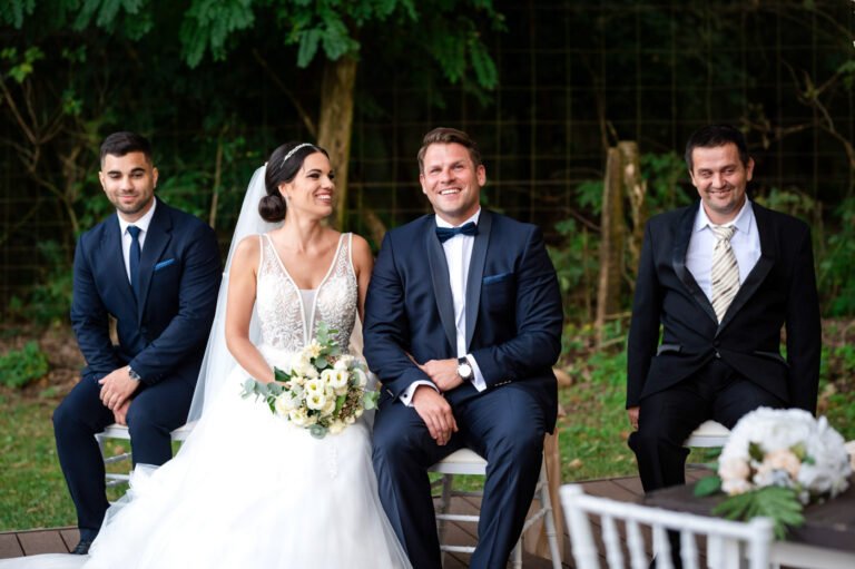 Boldog menyasszony és vőlegény elegáns esküvői öltözetben, mosolyogva a szertartás után. Esküvői fotózás természetközeli helyszínen.