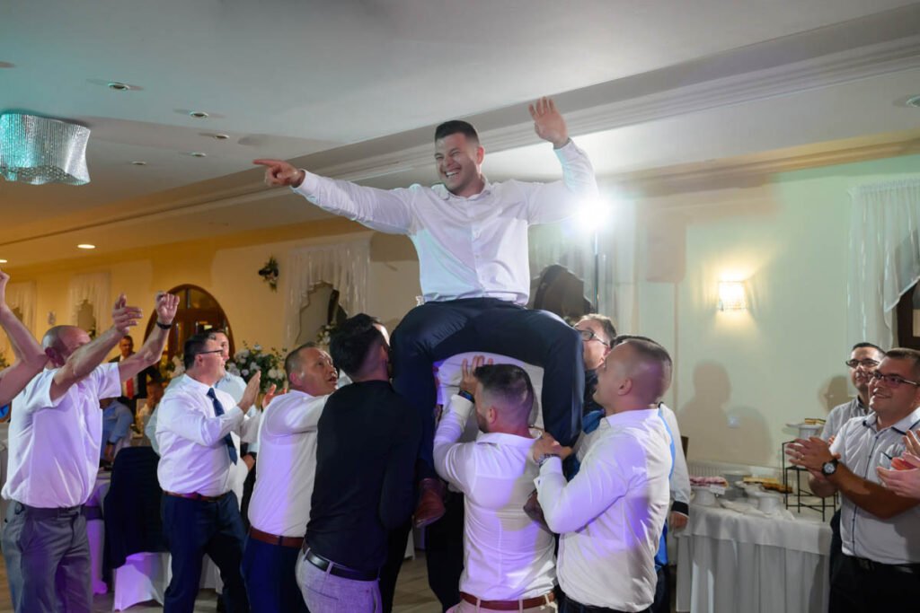 A férfi vendégek a magasba emelik a vőlegényt az esti mulatságon, a vendégsereg ünnepel körülötte